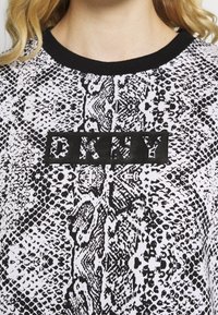 Šedá a bílá mikina s potiskem, která má design hadí kůže a černý obdélníkový logo s nápisem "DKNY" uprostřed. Černý kulatý výstřih.