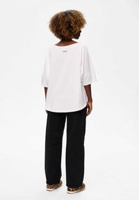 Biała, oversize'owa koszulka z szerokimi rękawami i okrągłym hemem, z małą metką z tyłu. W połączeniu z czarnymi spodniami o szerokich nogawkach i butami w zwierzęcy print.