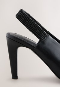 Scarpa décolleté nera in pelle con cinturino slingback arricciato e testurizzato, punta appuntita e tacco lucido a forma affusolata.