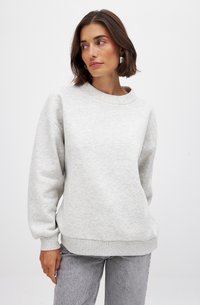 Lichtgrijze sweatshirt met een ronde hals, verlaagde schouders, ribgebreide boorden en een ribgebreide zoom. Zachte textuur, ontspannen pasvorm, gecombineerd met lichtgrijze jeans.