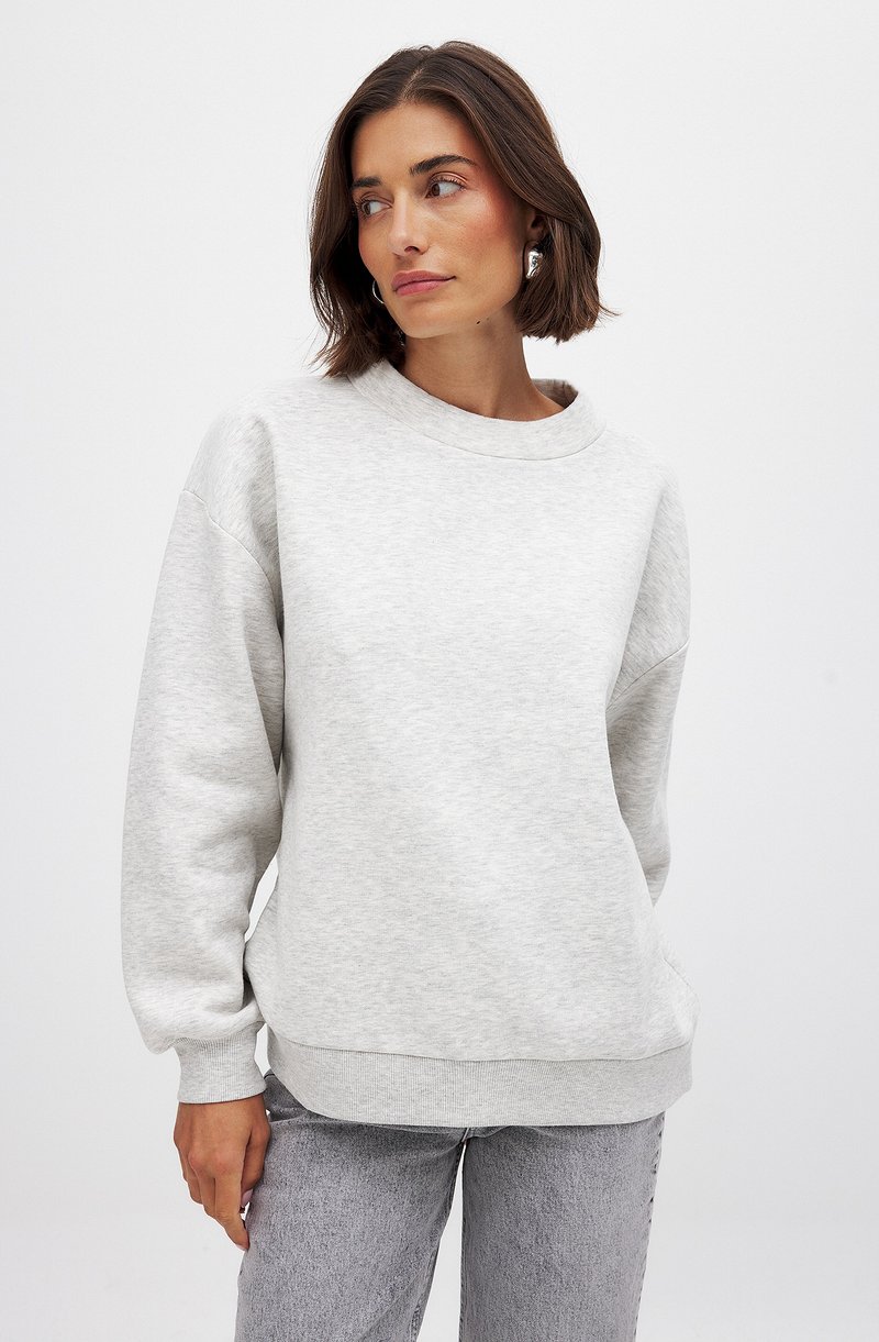 Lichtgrijze sweatshirt met een ronde hals, verlaagde schouders, ribgebreide boorden en een ribgebreide zoom. Zachte textuur, ontspannen pasvorm, gecombineerd met lichtgrijze jeans.