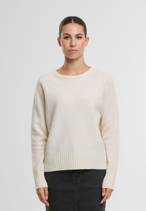 Cremfarbener Strickpullover mit rundem Ausschnitt, gerippten Bündchen und Saum sowie einer weichen Textur. Kombiniert mit einem dunklen Rock.