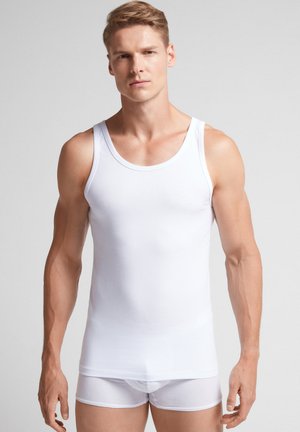 Weißes Tanktop aus glattem, leichtem Stoff mit rundem Ausschnitt und breiten Trägern, kombiniert mit weißen, figurbetonten Shorts.