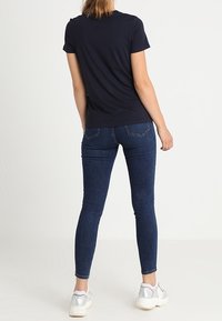 Námořnické tričko s krátkým rukávem spárované s tmavě modrými skinny džíny. Model nosí stříbrné tenisky, což podtrhuje uvolněný a přiléhavý vzhled zezadu.