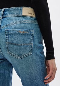 Μπλε τζιν παντελόνι από ντένιμ με ψηλή μέση και στενή εφαρμογή. Διαθέτει ταμπελάκι από δέρμα σε ταμπά χρώμα με την ένδειξη «Pepe Jeans» και μία πίσω τσέπη με κεντημένο λογότυπο.