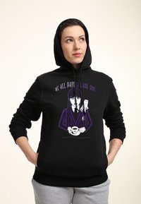 Felpa nera con cappuccio e design grafico che raffigura una figura che tiene una tazza e il testo "TUTTI ABBIAMO UN LATO OSCURO" in viola e bianco. Tessuto comodo.