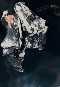 Fekete sportos tornacipők texturált anyaggal és hálós részletekkel, laza, batikolt mintájú nadrággal, fekete-fehér árnyalatokban.