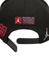 Cappello nero con logo "BRAND OF FLIGHT" in rosso, numero "23" ricamato in rosso e logo Jumpman grigio. Dotato di cinturino regolabile in plastica.