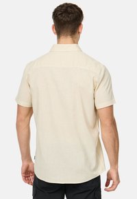 Korte mouwen shirt in lichtbeige stof met een gladde textuur en een kraag. Heeft een rechte zoom en zijsplitten, zonder zichtbare branding.