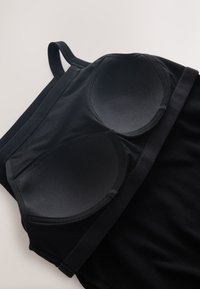 Brassière de sport noire rembourrée avec bretelles réglables et large bande élastique sous la poitrine, posée à plat sur une surface claire.