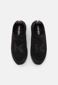 Zwarte instappers gemaakt van breimateriaal, met een rubberen zool, een gestructureerde bovenkant en een tonale 'K' logo aan de zijkant.