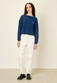 Felpa navy con vestibilità ampia e polsini a costine, abbinata a pantaloni larghi color crema e zoccoli neri con accenti blu.