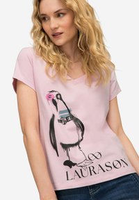 Camiseta de algodón rosa con escote en V, mangas cortas y un gráfico de un pájaro negro y rosa con el texto "LAURASON" impreso en la parte inferior.