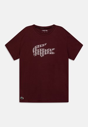 Mørk burgunder kortærmet T-shirt med en hvid geometrisk krokodille-logo centreret på brystet og et lille grønt krokodilleemblem nær kanten.