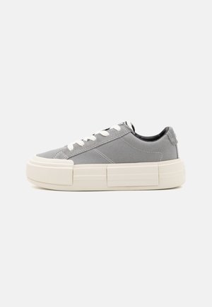 Zapatillas de lona gris de caña baja con cordones blancos y suela de goma gruesa de color blanco roto con acentos rectangulares texturizados.
