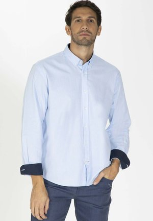 Chemise bleu clair à manches longues et poignets navy. Fabriquée en tissu doux, elle présente un col et des boutons sur le devant.