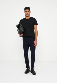 Black v-neck t-shirt, navy tailored trousers, and black leather shoes. Model holds a black leather bag. Simple design, smooth texture.
