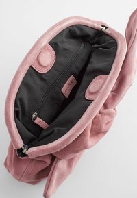 Pink suede handbag with a black fabric interior, featuring a zippered pocket and snap closures, designed in a soft, rounded shape.