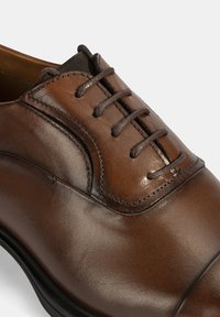 Bruine leren schoenen met een gladde afwerking, ronde neus en zes veterogen met bruine veters. Subtiele stikaccenten verbeteren het ontwerp.