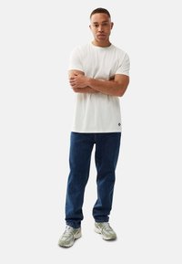 Vit t-shirt med kort ärm och rund halsringning, ihopparad med blå denimjeans och ljusgröna sneakers med texturerade accenter.