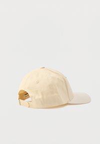 Beżowa bawełniana czapka baseballowa z lekko wygiętym daszkiem, regulowanym paskiem z tyłu i otworami wentylacyjnymi.