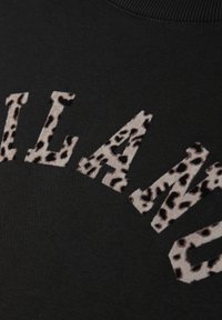 Sudadera negra con letras texturizadas de estampado de leopardo en beige y marrón. Tela suave con escote redondo y puños acanalados.