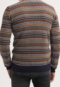 Pull en tricot présentant un motif géométrique multicolore dans des tons terreux, avec une bordure côtelée bleu marine aux ourlets et aux poignets, des manches longues et un col rond.