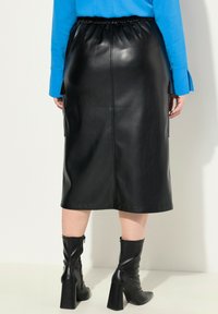 Gonna midi in finta pelle nera con una vita elastica, abbinata a stivali neri con tacco alti fino al ginocchio, che evidenziano una texture liscia e raffinata.