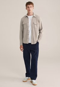 Cămașă butonată de un gri deschis cu două buzunare la piept, purtată peste un tricou alb. Asortată cu pantaloni bleumarin închis și adidași deschiși cu accente verzi.
