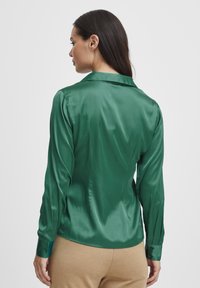 Grüne Satin-Hemd mit langen Ärmeln, Kragen und geknöpften Manschetten. Hat eine glatte Textur und eine figurbetonte Passform, mit einem taillierten Rücken.