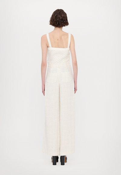 Weißes zweiteiliges Outfit mit einem strukturierten schulterfreien Oberteil und weit geschnittenen Hosen mit Gesäßtaschen. Slingback-Absätze vervollständigen den Look.