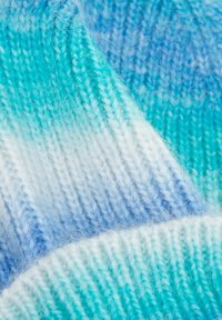 Gorro de punto en tonos degradados de turquesa y azul, con una tela suave y texturizada que presenta diferentes puntos y un dobladillo enrollado.