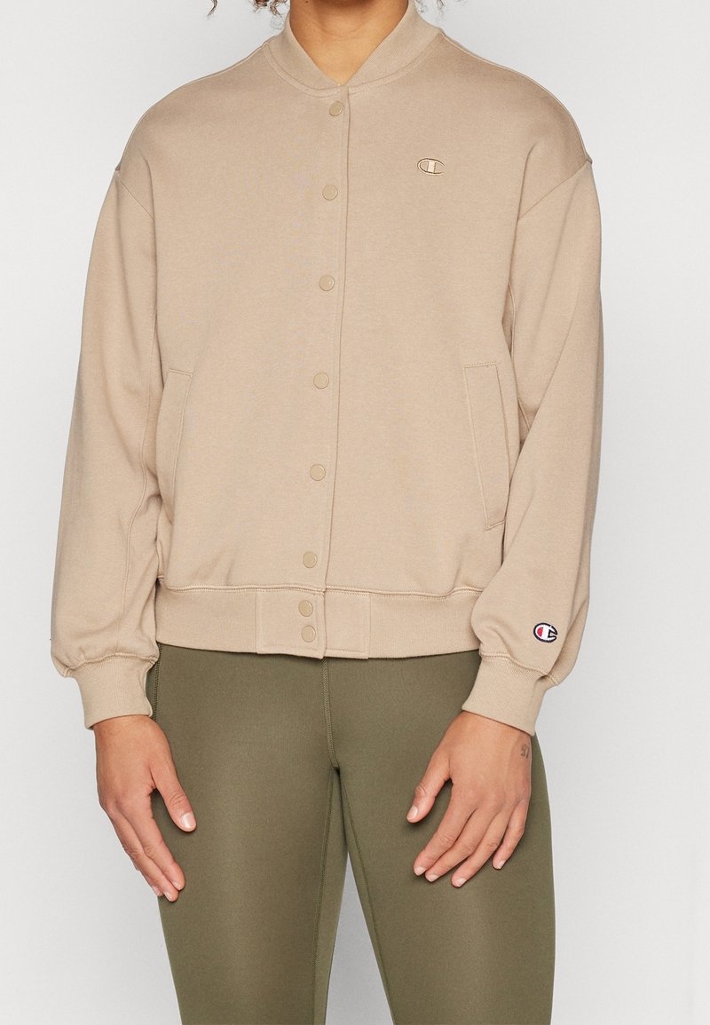 Giacca felpata beige con chiusura a bottoni, polsini e orlo a coste. Realizzata in tessuto morbido, presenta un piccolo logo sulla manica sinistra.