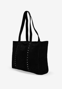 Bolso tote de ante negro con dos asas largas, que presenta filas verticales de tachuelas plateadas en la parte delantera. Forma rectangular, textura suave.