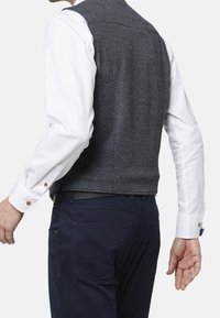 Grå texturerad väst med en figursydd design, tillsammans med en vit långärmad skjorta med en subtil mönstring och knappdetaljer.