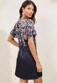 Kukallioinen mekko, jossa on lyhyet pleated-hihat, tummansininen pohjaväri ja hieman teksturoitu kangas. Takana on avainreikäyksityiskohta.