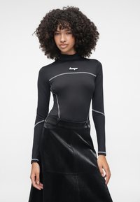 Camisola preta de mangas longas com gola alta e costura prateada, combinada com uma saia preta de imitação de pele texturizada com padrão de cobra.