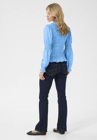 Top blu smockato con lunghe maniche a sbuffo, abbinato a jeans a zampa scuri e ballerine nere. Texture liscia con orlo arricciato.