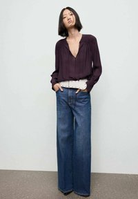 Langærmet bluse i blommefarve med dyb V-hals og indsamlede skuldre, parret med lysfarvede, vide denim jeans med bindebælte og bæltesløjfer.