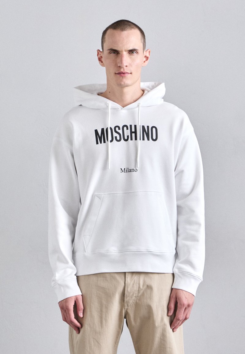 Hanorac alb din bumbac, cu un logo mare negru "MOSCHINO" și un text mai mic "Milano", dotat cu buzunar tip cangur și glugă cu șnur.