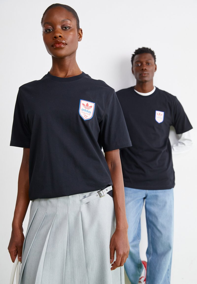 Melnas īsām piedurknēm t-krekli ar sarkano un zilo Adidas logo uzšišanu, ar klasisku piegriezumu. Viens modelis valkā pelēku svārku ar krokām.