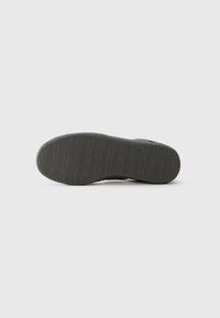 Suola di scarpa con grip a motivo che presenta il testo ripetuto "Jack & Jones" su uno sfondo bianco.')}}}]}