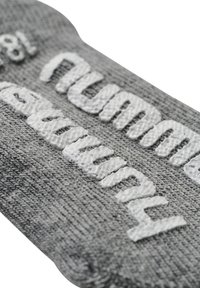 Graues Textillabel mit erhabenen weißen Text. Der Stoff hat eine strickartige Textur mit einer glatten Oberfläche und abgerundeten Kanten.