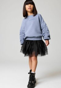 Sudadera azul con mangas recogidas, falda de tul negra y botas de combate negras. El suéter presenta el texto bordado "ALLSAINTS."
