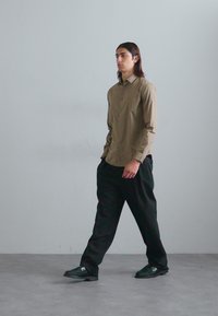 Hellbraunes Button-Up-Hemd, schwarze lockere Hose und dunkle Sneakers. Glattes Material, lässiges Design und minimalistischer Stil.