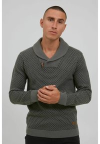 Suéter gris de punto con un patrón texturizado, cuello de chal y detalle de botón de madera en el escote. Puños y dobladillo ajustados.