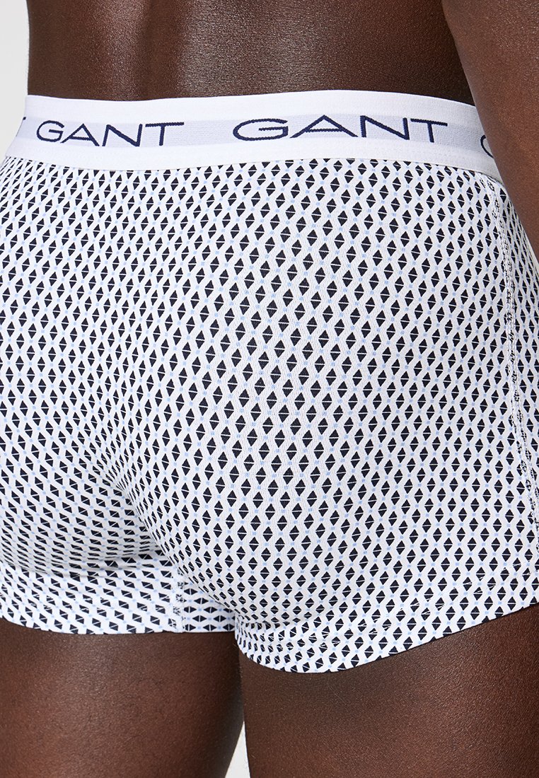 Nahaufnahme einer Person in weißen Boxershorts mit einem schwarzen Diamantmuster und einem weißen Taillengummibund, der mit "GANT" markiert ist.