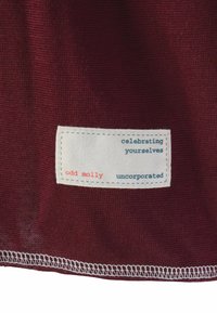 Bordo tkanina s malom bijelom etiketom na kojoj se nalaze plavi i crveni tekst koji govori "odd molly", "slavite sebe" i "nedjeljivo".