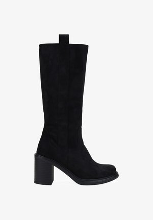 Bota de ante negra hasta la rodilla con punta cuadrada y tacón bloque. Presenta paneles laterales elásticos y un tirador para facilitar su uso.