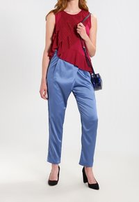 Červený bezrukávový top s plisovaným designem, spárovaný se světle modrými saténovými zúženými kalhotami a černými vysokými podpatky. Součástí je malá černá kabelka.